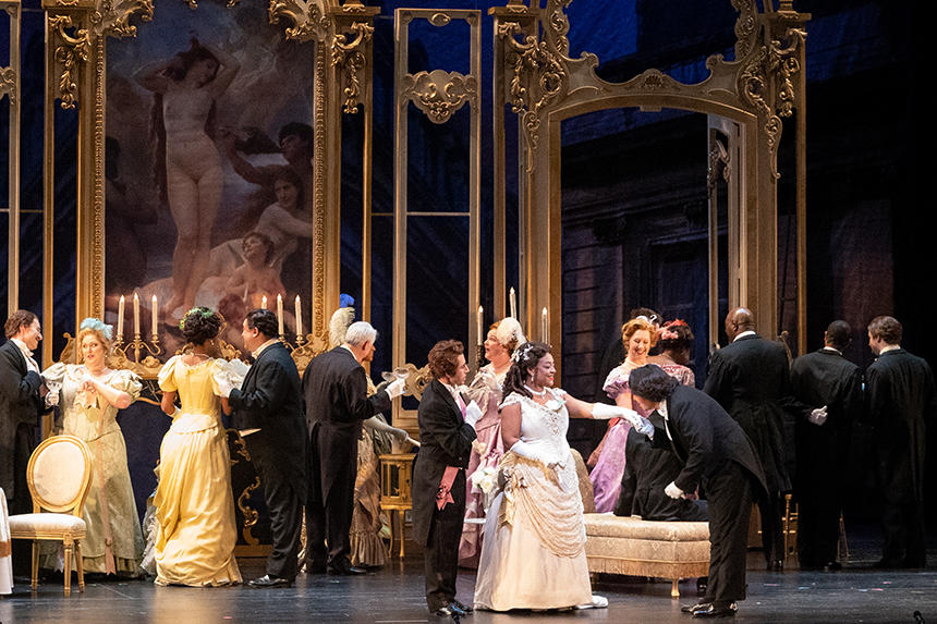 A festive party scene from Virginia Opera's La Traviata, with an ornate, gold-trimmed ballroom full of gown- and tuxedo-wearing guests.