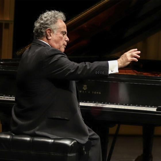 Jeffrey Siegel performs at a grand piano, right arm outstretched over the keys.
